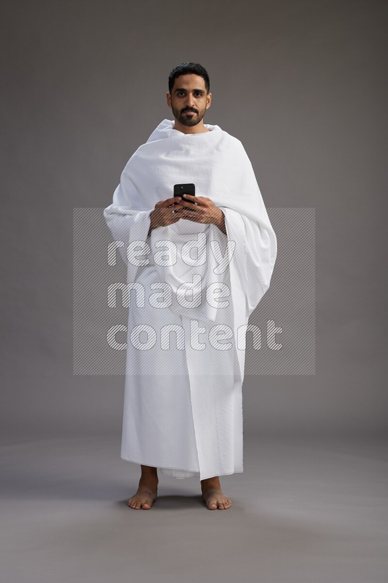 A man wearing Ehram Standing texting on phone on gray background