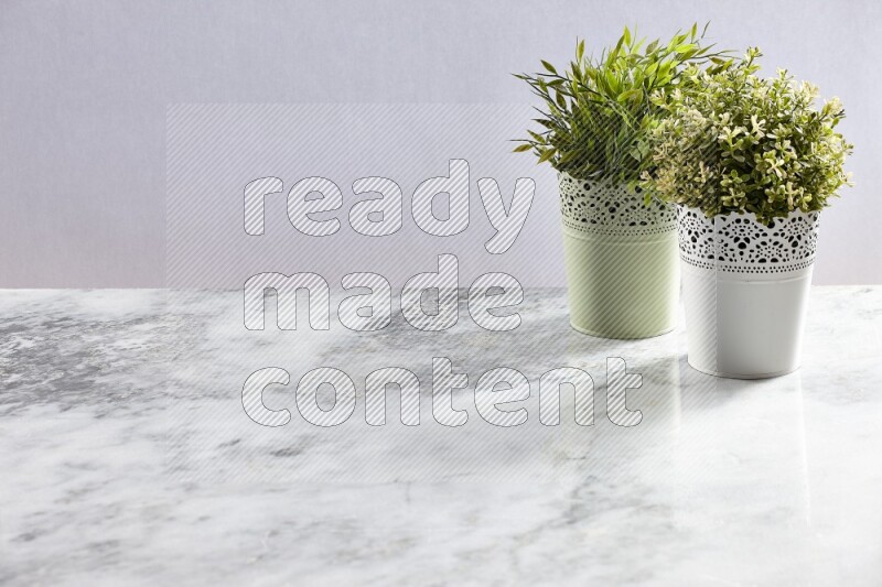 Two different artificial plants in white and green decorative pots on grey marble background