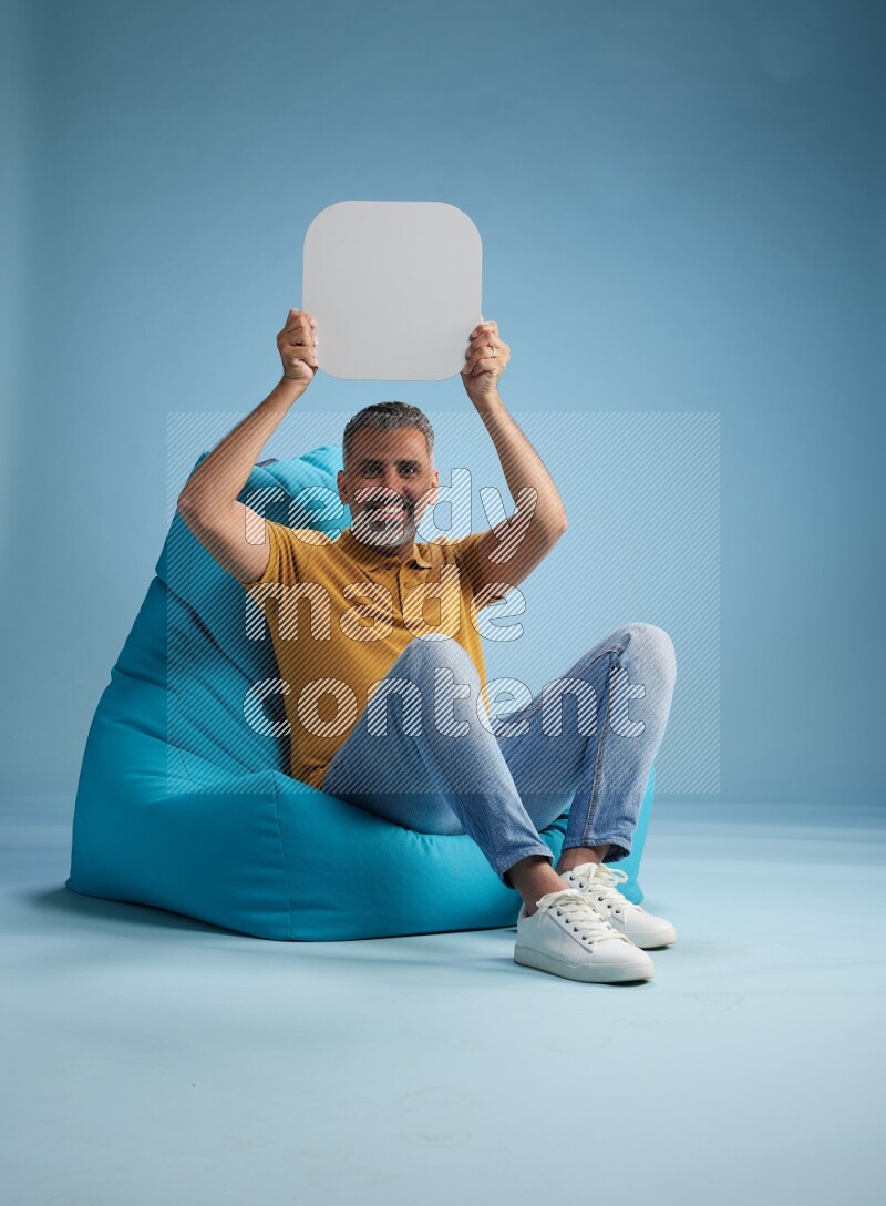 A man sitting on a blue beanbag and holding social media sign