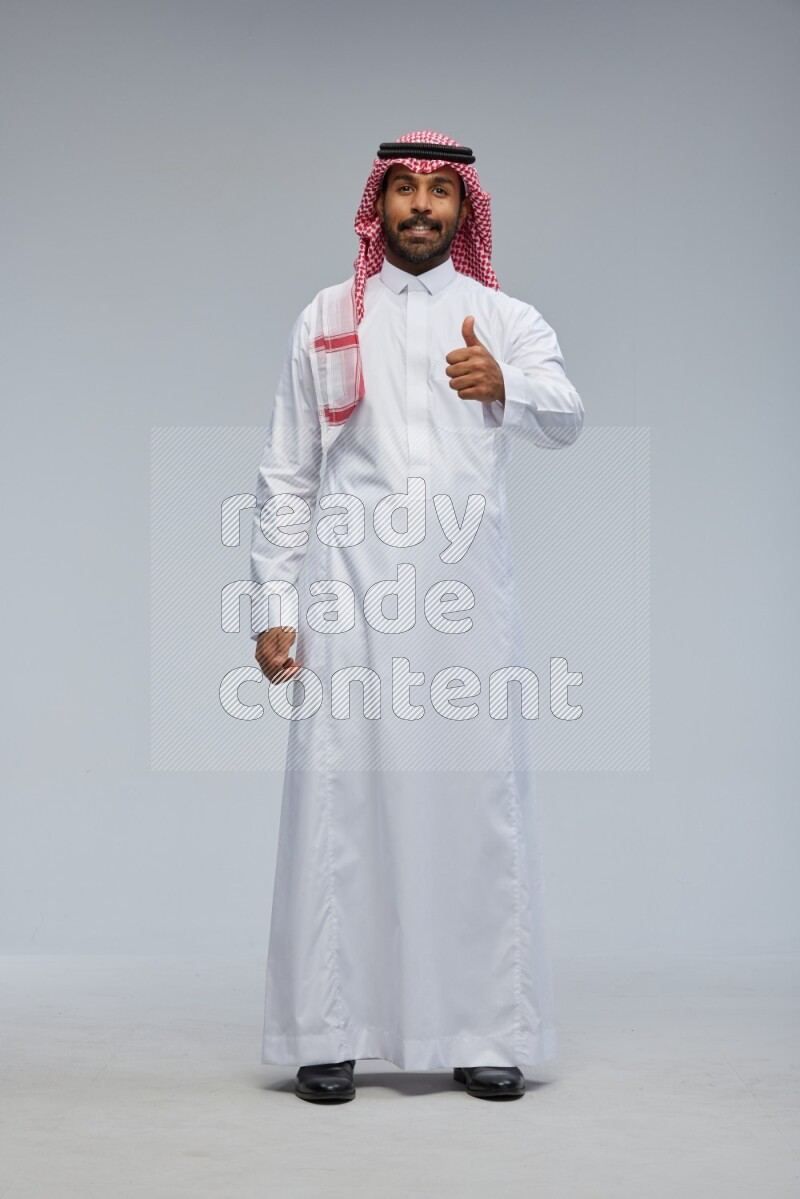 Saudi man Wearing Thob and shomag standing interacting with the camera on Gray background