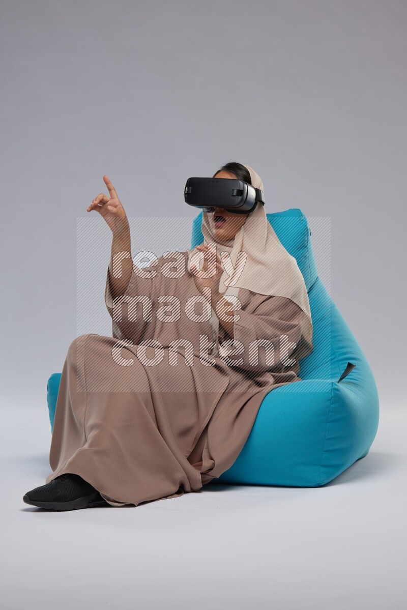 A Saudi woman sitting on a blue beanbag and gaming with VR