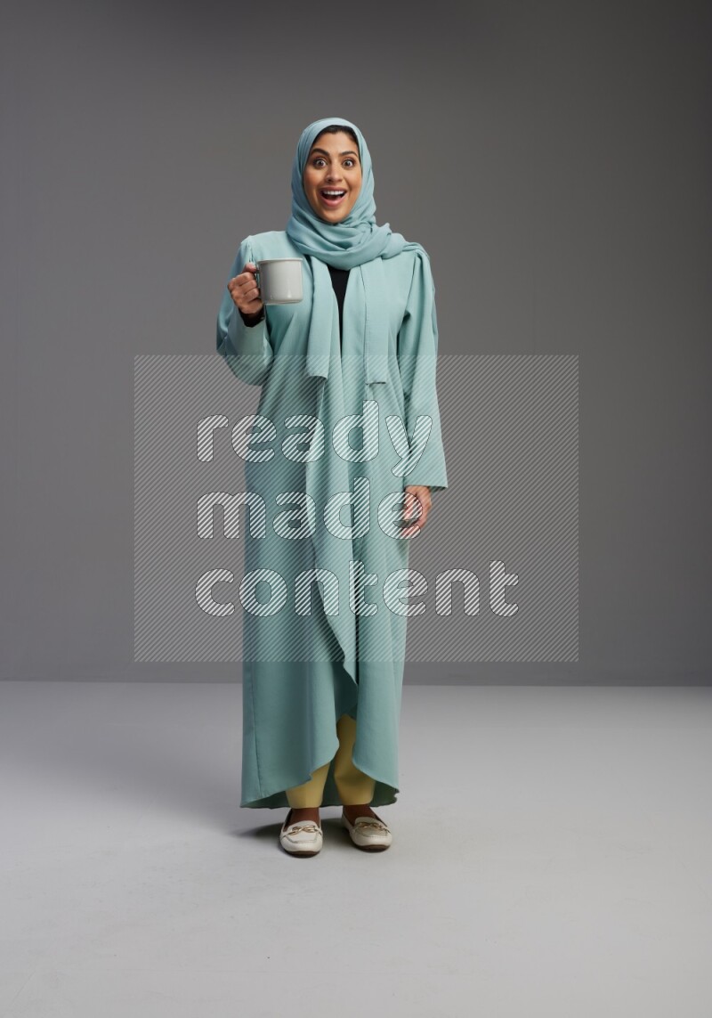 Saudi Woman wearing Abaya standing  holding a mug on Gray background