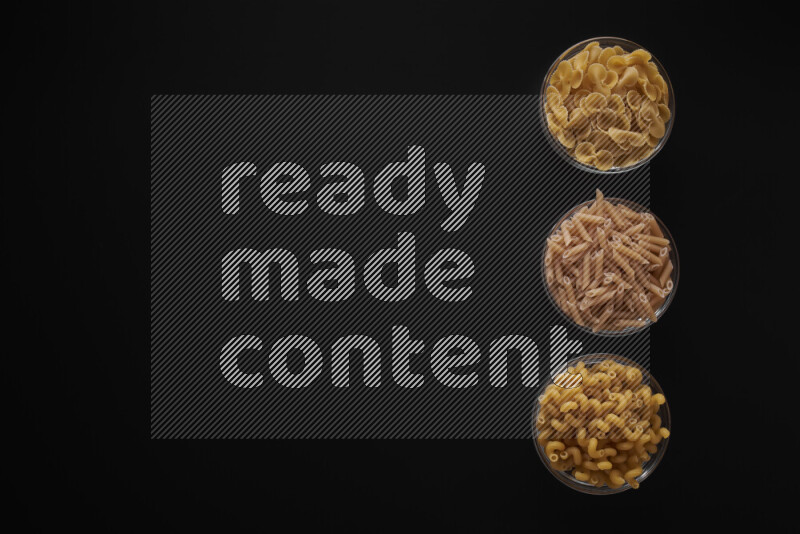 Different pasta types in 3 glass bowls on black background