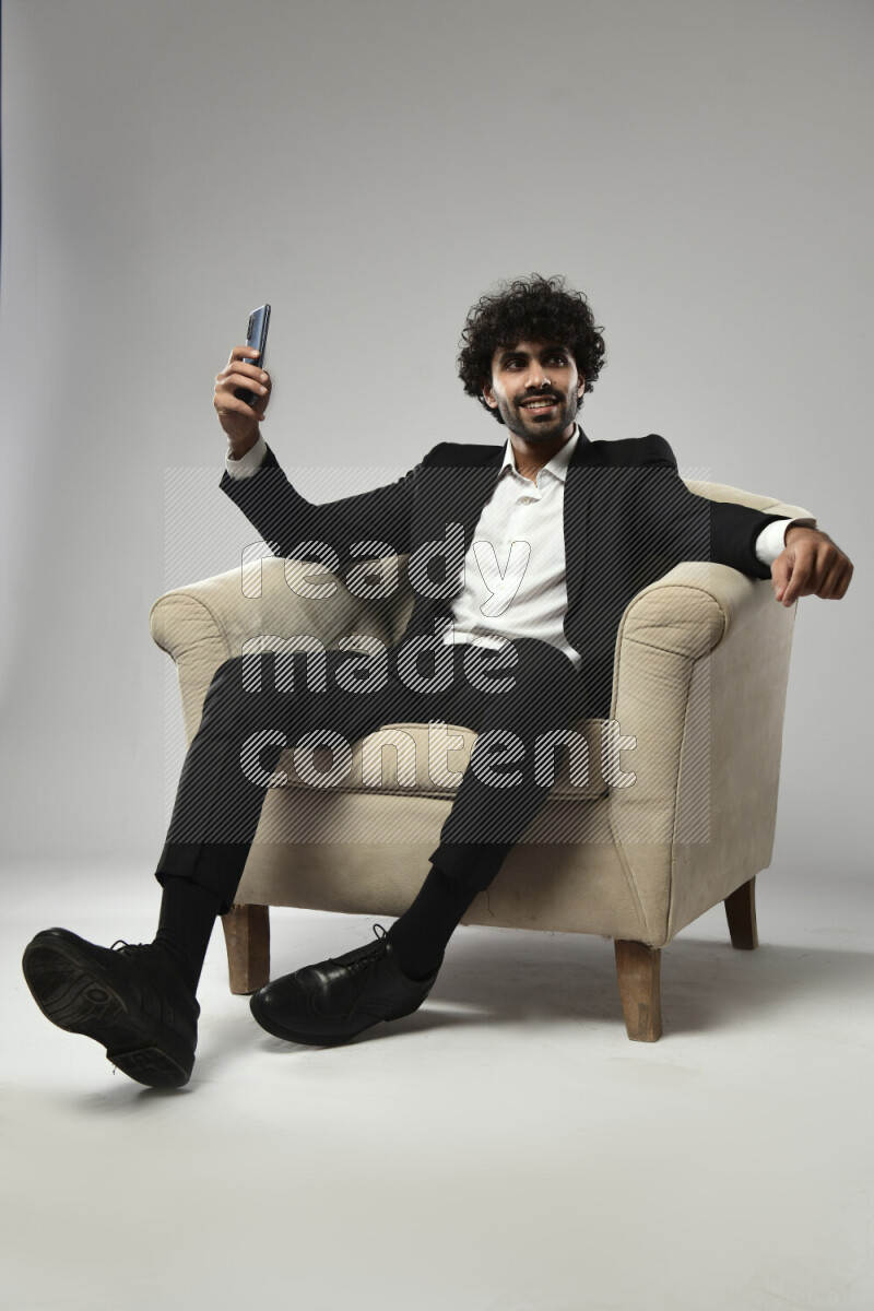 A man wearing formal sitting on a chair taking a selfie on white background