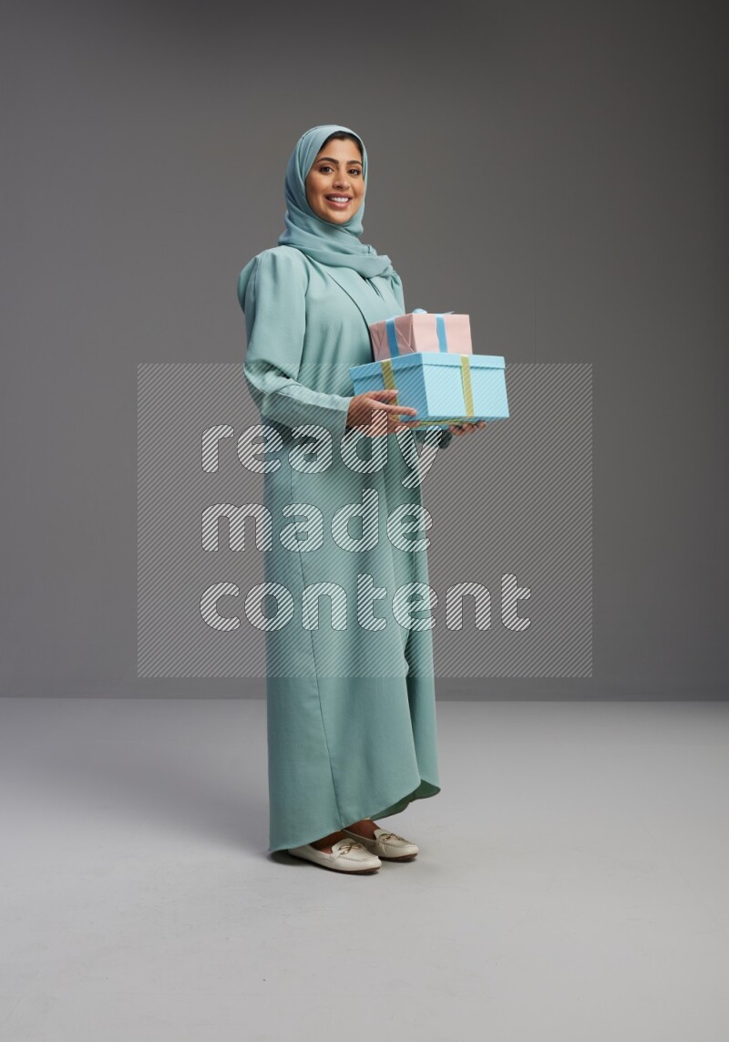 Saudi Woman wearing Abaya standing holding gift box on Gray background