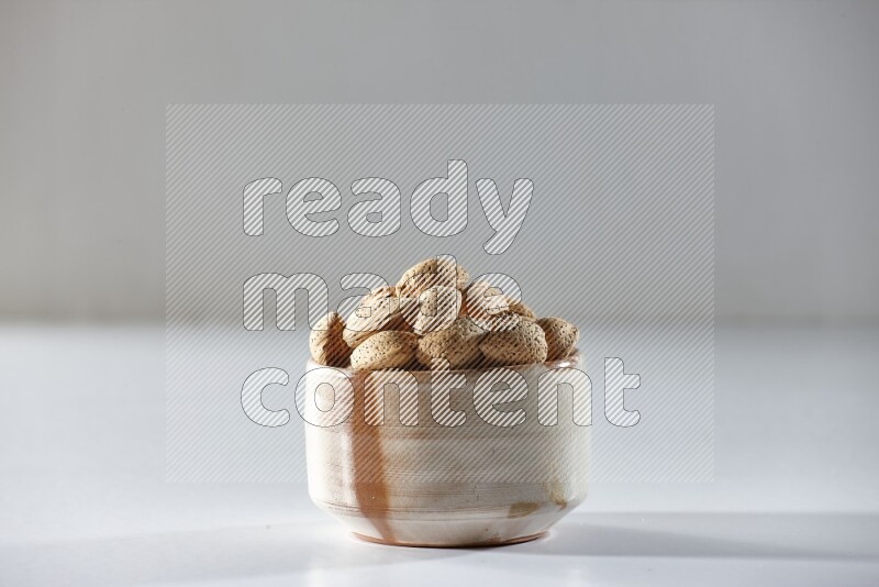 A beige ceramic bowl full of almonds on a white background in different angles