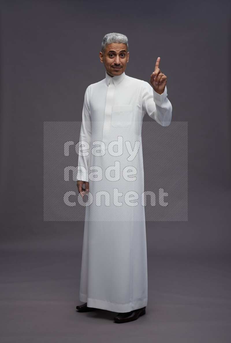 Saudi man wearing thob standing interacting with the camera on gray background