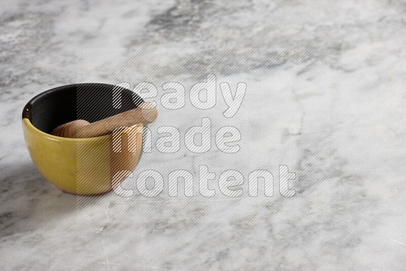 Multicolored pottery bowl with wooden honey dipper in it on grey marble background