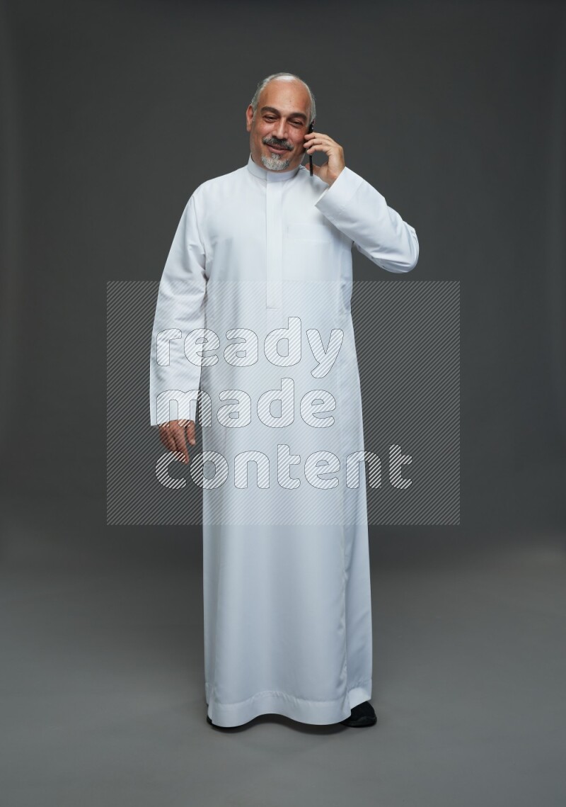 Saudi man without shomag Standing talking on phone on gray background