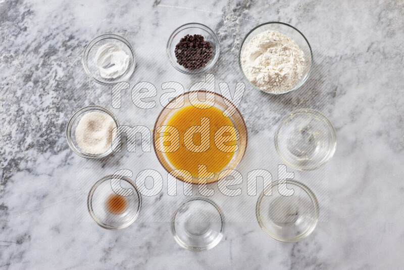 كوكيز خطوة بخطوة بمكوناتها، الدقيق، الزبدة، السكر البني، البيض، الفانيليا، السكر الأبيض، رقائق الشوكولاتة وصودا الخبز على خلفية رخام رمادي