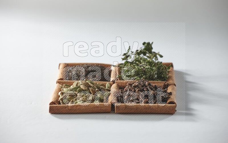 4 مربعات من أعواد القرفة ممتلئة بالشاي والهيل والنعناع والقرنفل على أرضية بيضاء