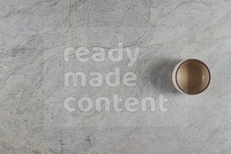 A small beige pottery bowl on grey marble background