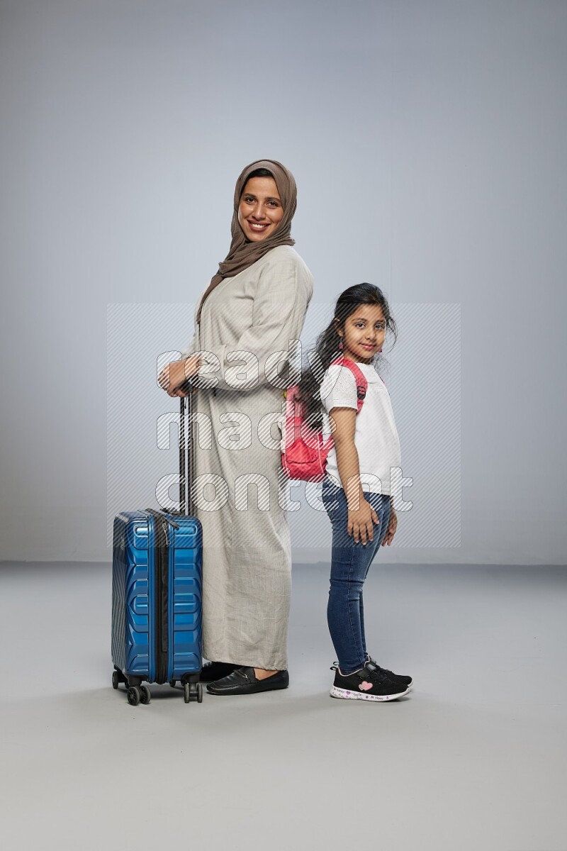 Mom and daughter standing pulling a carry-on bag on gray background