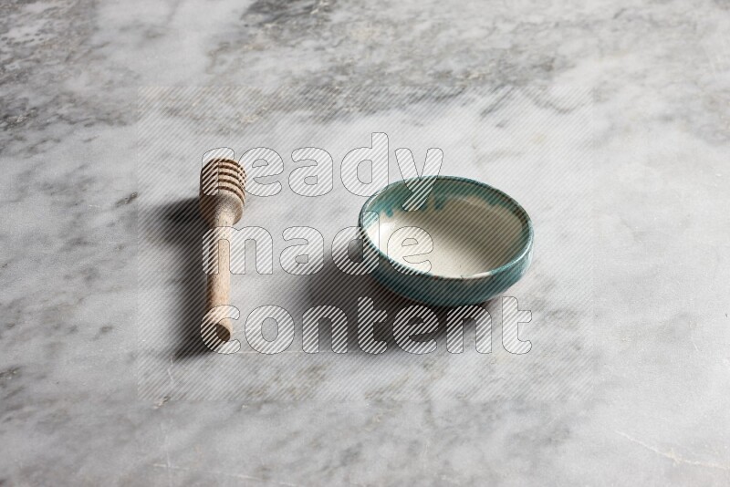 Multicolored pottery bowl with wooden honey dipper on the side on grey marble background