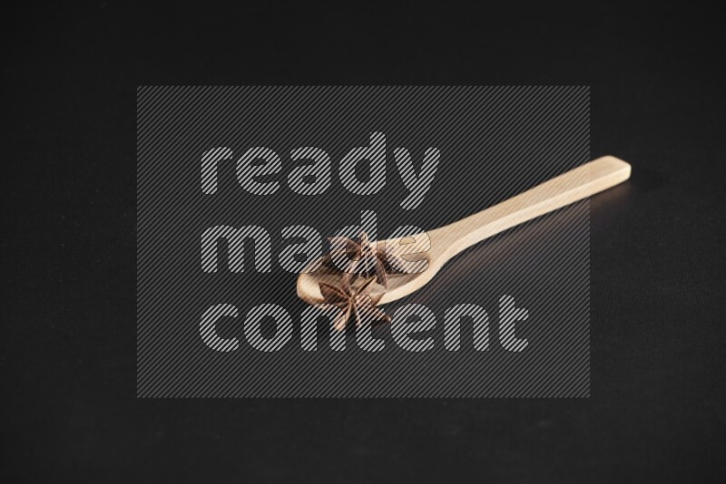 Star Anise in a wooden spoon on more stars anise filling the frame on black flooring