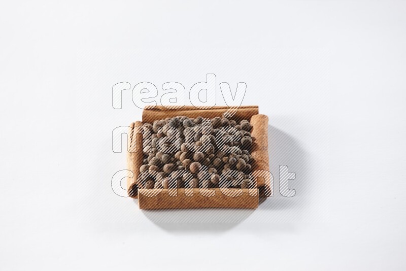 أربعة من أعواد القرفة مكونة شكل مربع بداخلها بهار الفلفل الحلو علي خلفية بيضاء