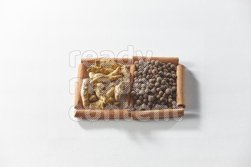 مربعان من أعواد القرفة ممتلئان ببهار الفلفل الحلو وأصابع الكركم علي خلفية بيضاء