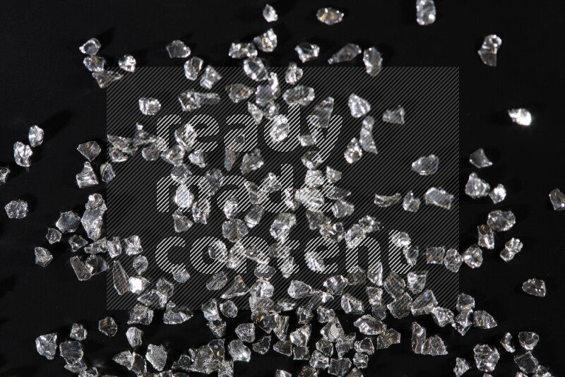 Silver shimmering fragments of glass scattered on a black background
