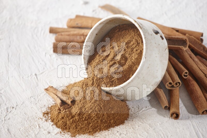 Ceramic beige bowl over filled with cinnamon powder and cinnamon sticks around the bowl on a textured white background in different angles