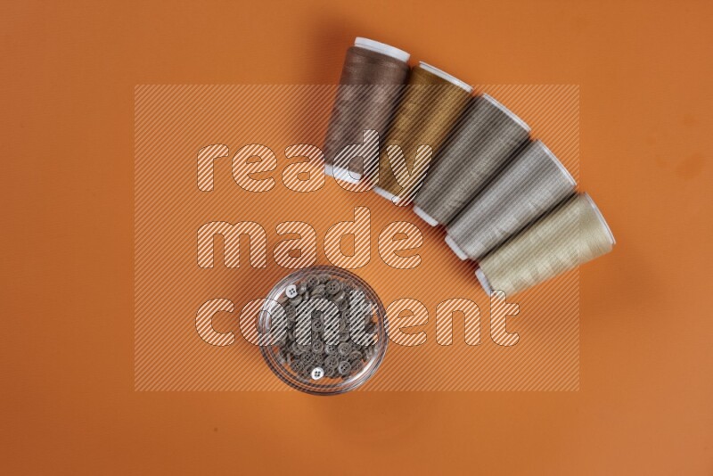 مجموعة من أدوات الخياطة والتفصيل بنية اللون على خلفية برتقالية