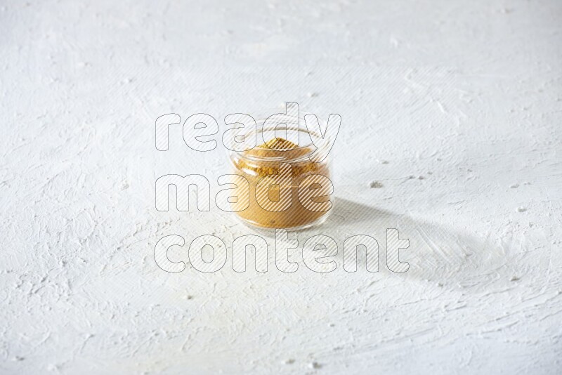 A glass jar full of turmeric powder on a textured white flooring