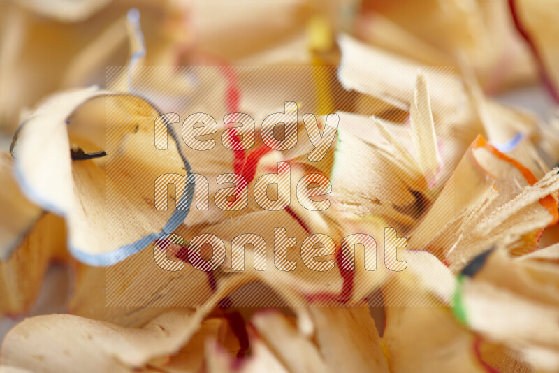 A close-up showing a small pile of pencil shavings with varied color edges on grey background
