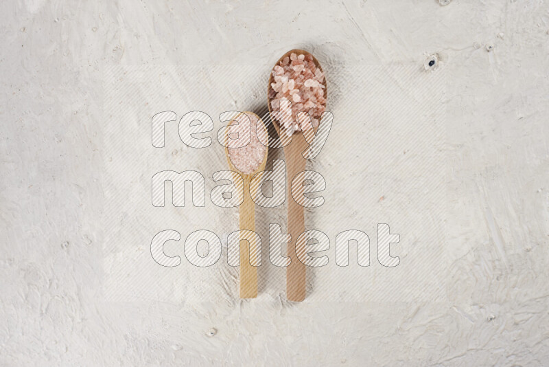2 wooden spoons filled with fine and coarse salt on white background