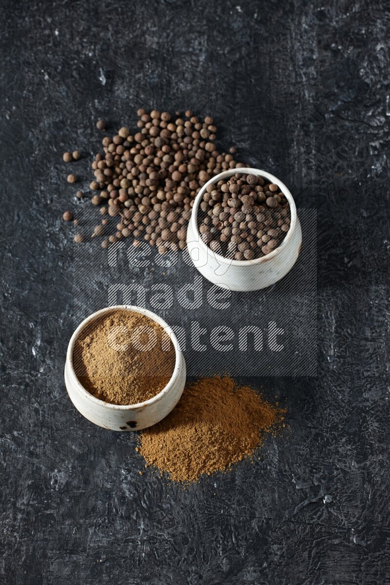 2 beige bowls, one full of allspice powder and the other full of whole balls and both spread on a textured black flooring