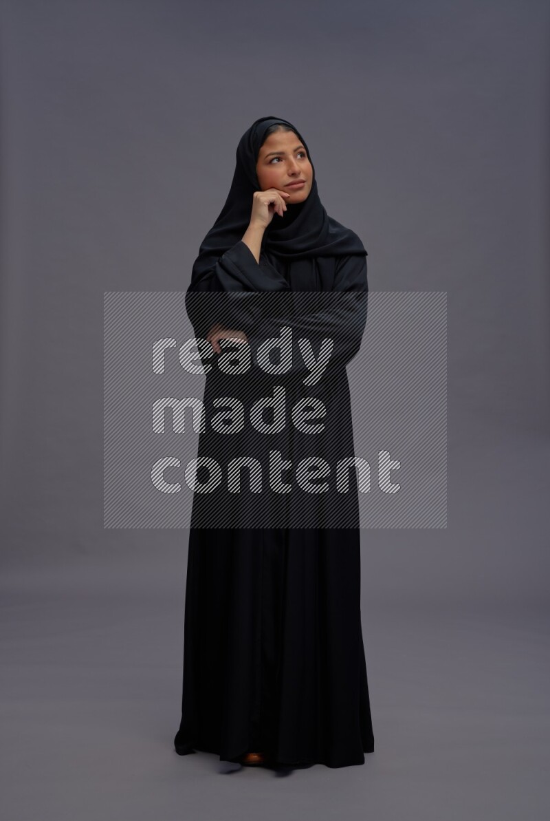 Saudi woman wearing Abaya standing interacting with the camera on gray background