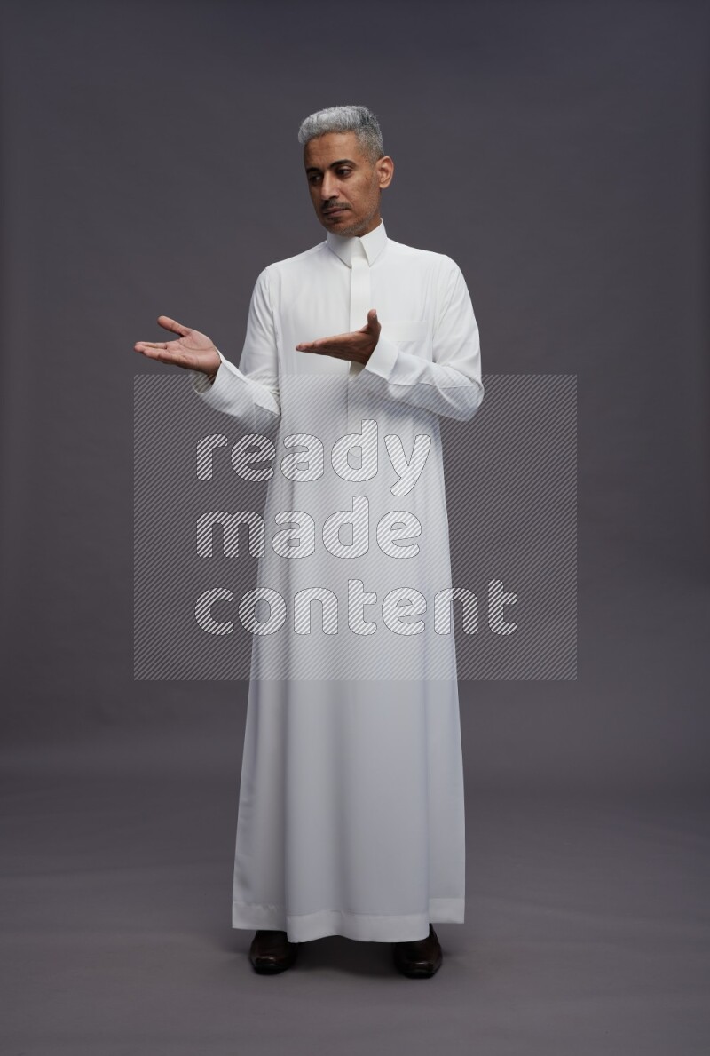 Saudi man wearing thob standing interacting with the camera on gray background