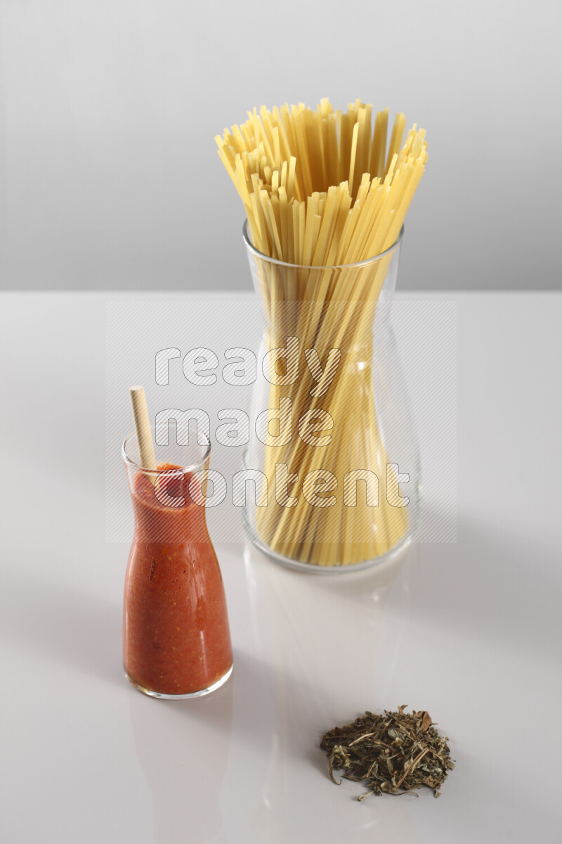 Raw pasta with tomatoe pasta with different ingredients such as cherry tomatoes, basil, garlic, bay laurel, cardamom, white pepper, black pepper, red chilis and wheat stalks on light grey background