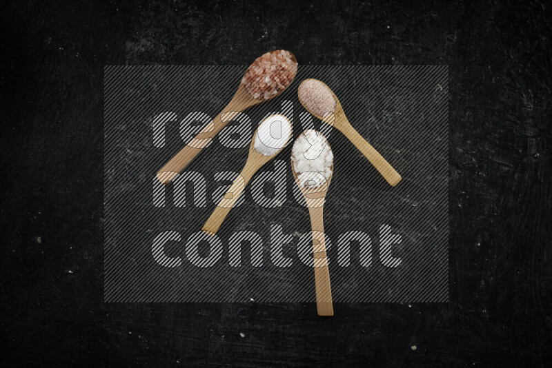 4 wooden spoons filled with fine and coarse salt on black background