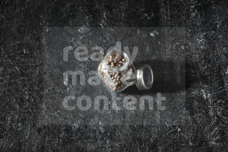 وعاء زجاجي للتوابل ممتلئ بحبوب بهار الفلفل الحلو منه على خلفية سوداء