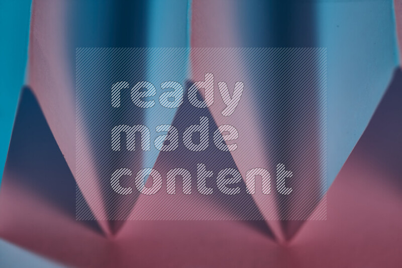 A close-up abstract image showing sharp geometric paper folds in blue and pink gradients