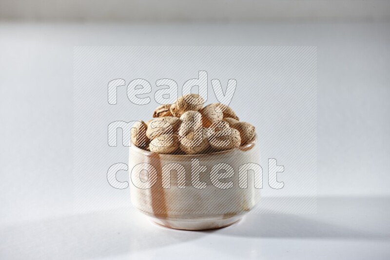 A beige ceramic bowl full of almonds on a white background in different angles
