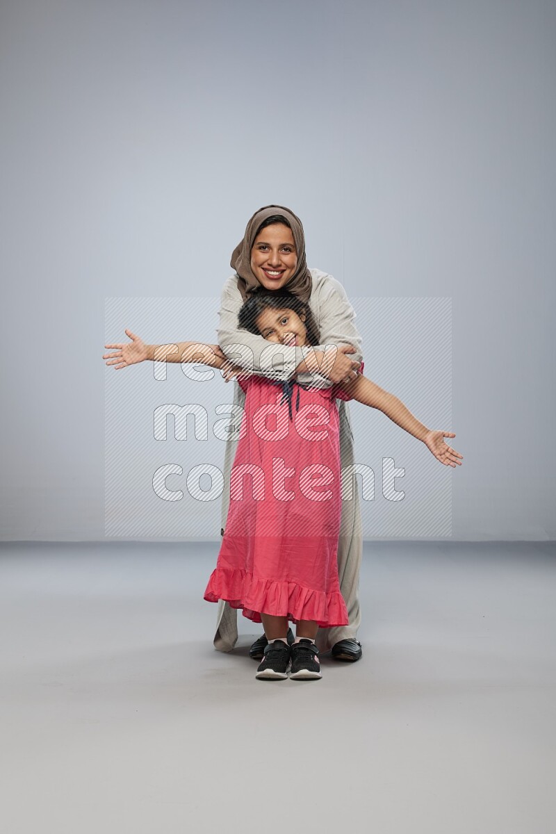 A girl and her mother interacting with the camera on gray background