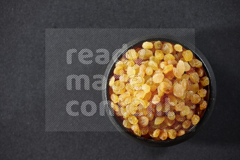 A black pottery bowl full of raisins on a black background in different angles