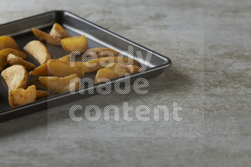 wedges potato in a black stainless steel rectangle tray on grey textured counter top