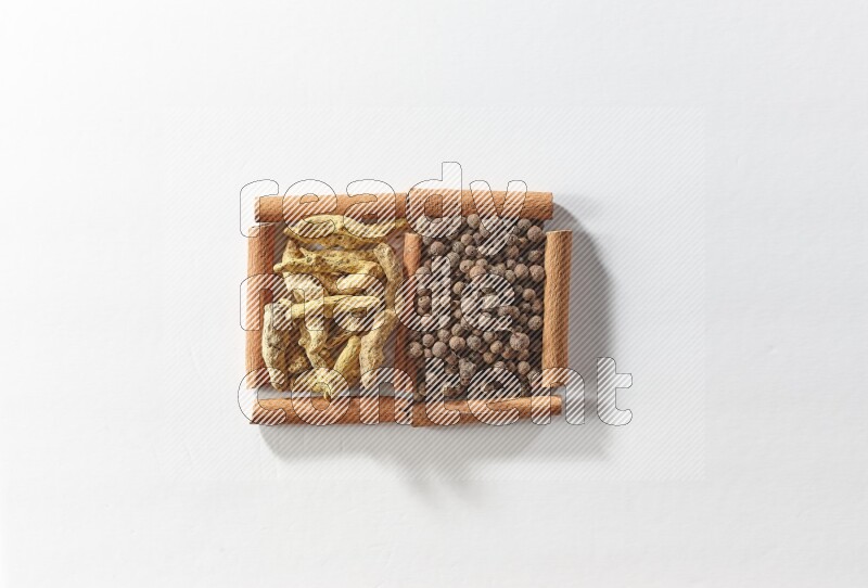 مربعان من أعواد القرفة ممتلئان ببهار الفلفل الحلو وأصابع الكركم علي خلفية بيضاء