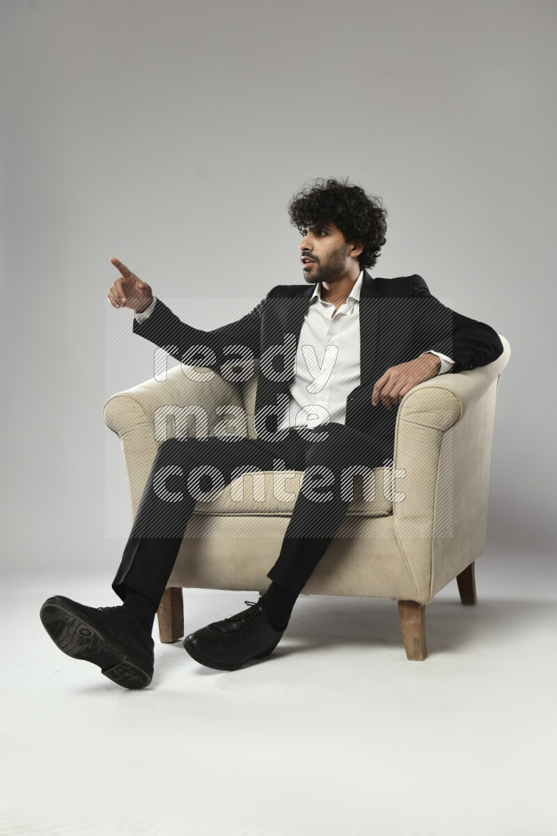 A man wearing formal sitting on a chair making a hand gesture on white background