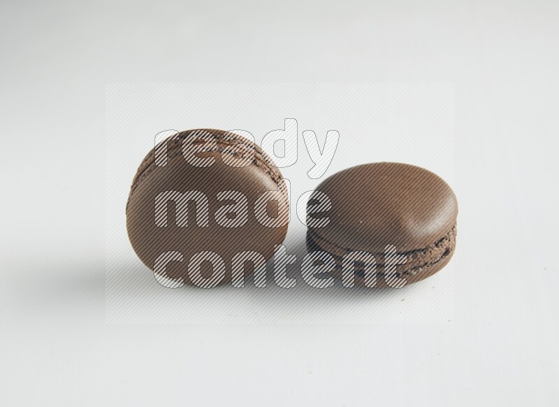 45º Shot of two Brown Dark Chocolate macarons on white background
