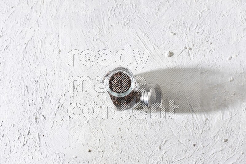 A glass spice jar full of cloves on textured white flooring