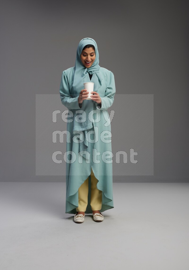 Saudi Woman wearing Abaya standing  holding paper cup on Gray background