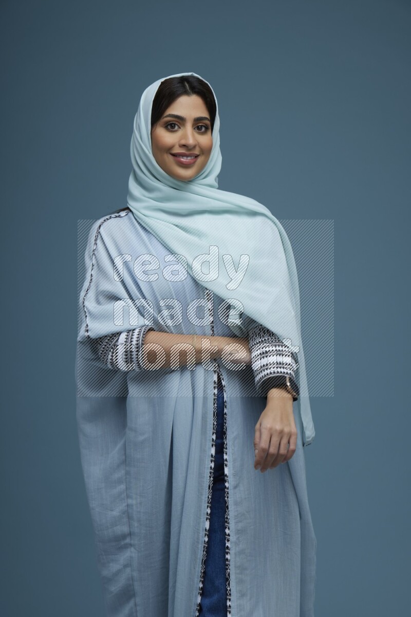 A woman posing in a blue background wearing a blue Abaya with hijab
