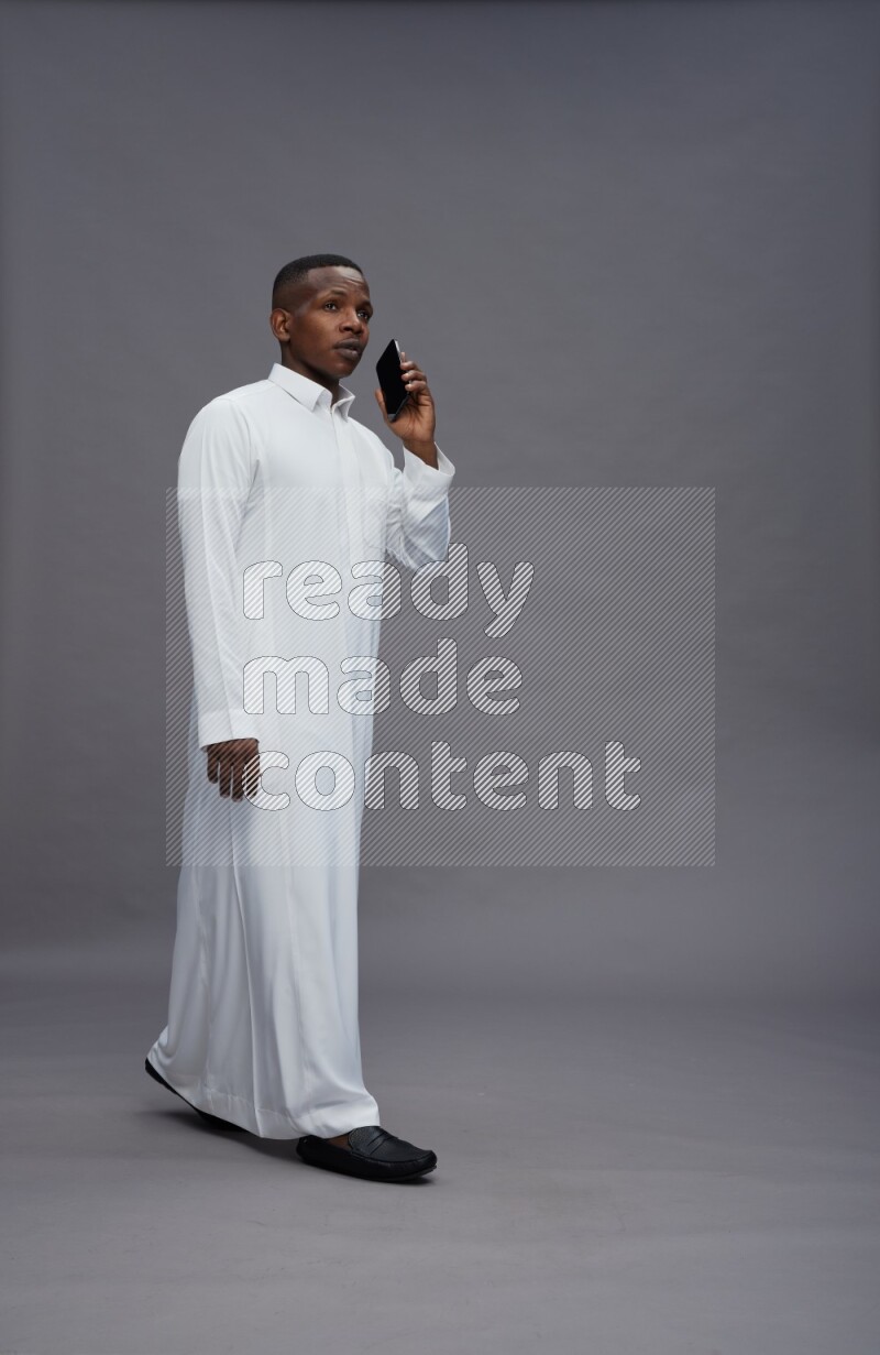 Saudi man wearing thob standing talking on phone on gray background