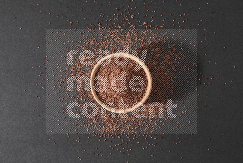 وعاء خشبي ممتلئ ببذور حب الرشاد محاط ببعض البذور علي خلفية سوداء