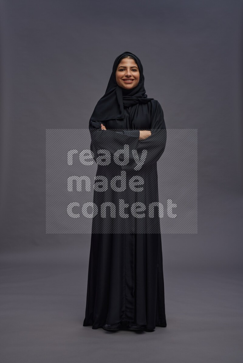 Saudi woman wearing Abaya standing with crossed arms on gray background