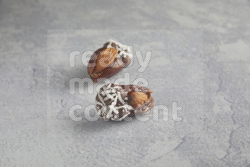 Two Almond stuffed dates covered with dark chocolate and coconut on a light grey background