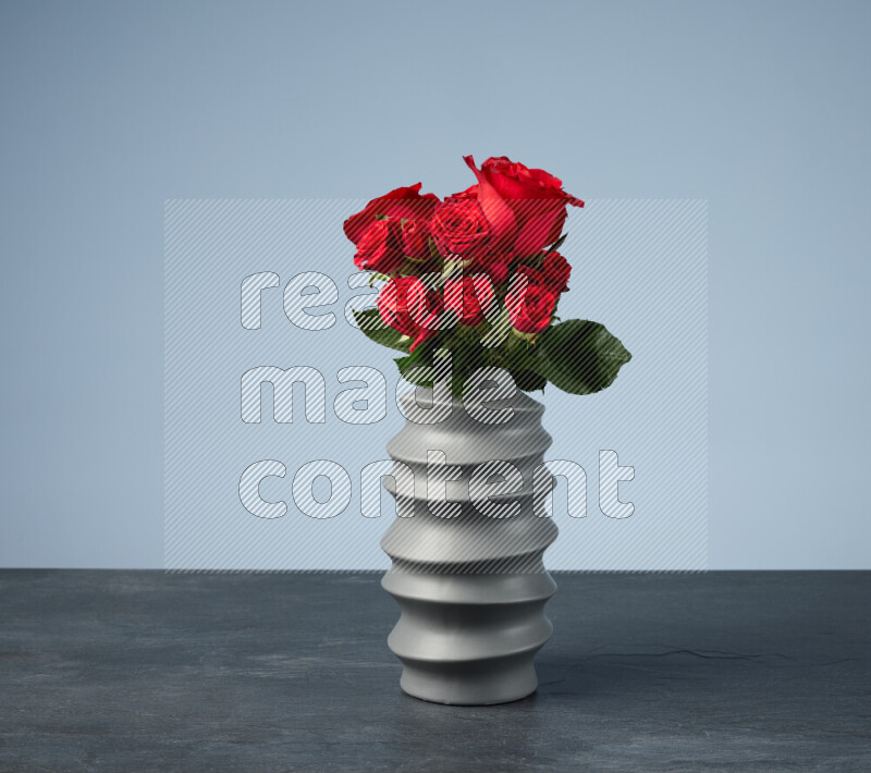 An arrangement of vivid red roses in a grey spiral vase on black marble background