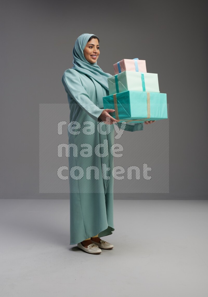 Saudi Woman wearing Abaya standing holding gift box on Gray background